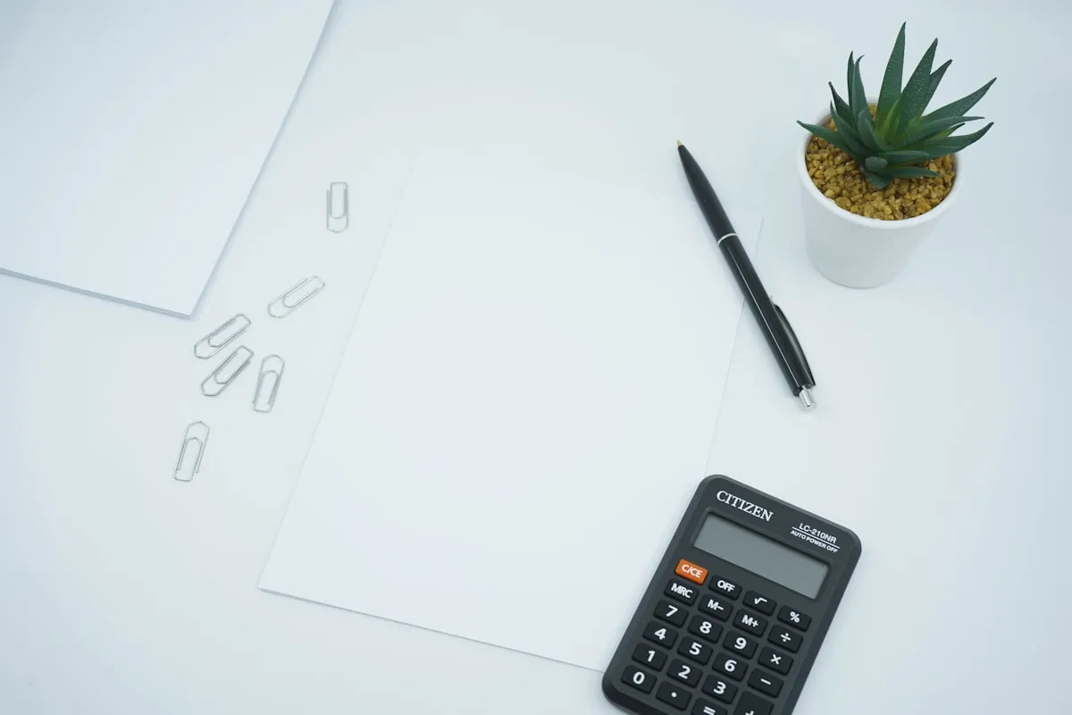 Calculadora preta, caneta e folhas de papel em branco sobre mesa de escritório